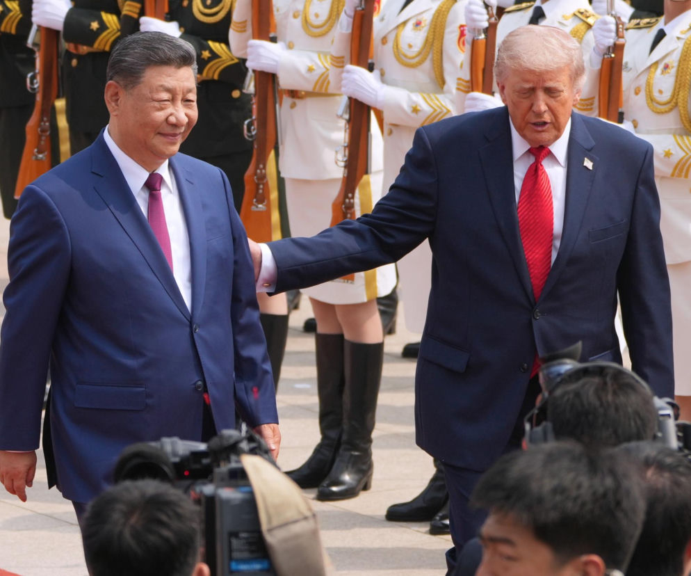 Prezydenci Donald Trump i Xi Jinping w garniturach, z ochroniarzami w tle, podczas spotkania w Pekinie. Trump z ręką na ramieniu Xi, co symbolizuje pozytywne rozmowy między USA i Chinami, wpływające na rynki ropy. Więcej na Super Biznes.