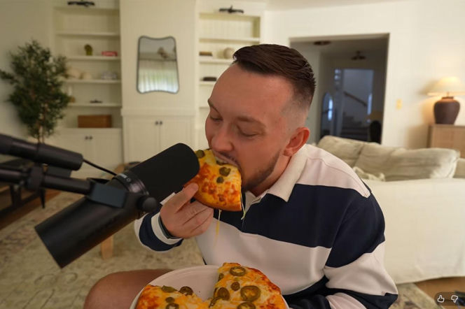 Książulo je pizzę z dodatkiem papryczek jalapeño przed profesjonalnym mikrofonem. O jej składzie przeczytasz na PZ Fit.