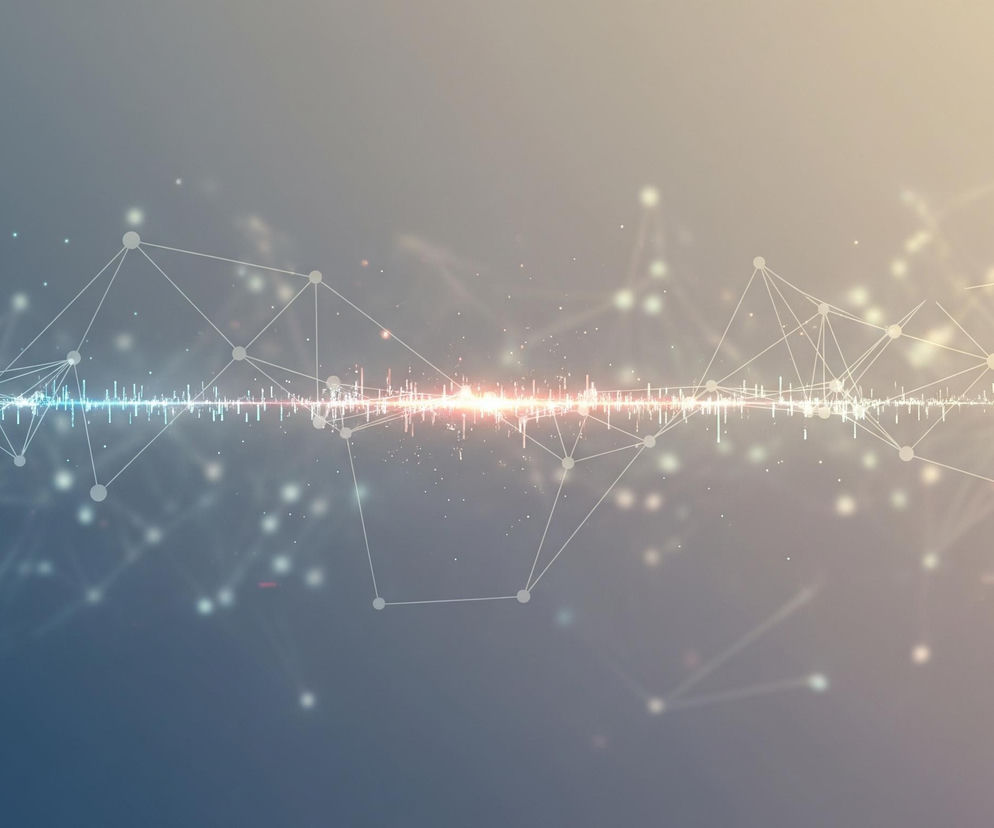 Abstrakcyjna grafika przedstawia dynamiczną sieć połączeń z elementami audio i świetlnymi na tle gradientowym. Centralną część obrazu zajmuje pozioma linia składająca się z migoczących pionowych słupków o różnej wysokości, symbolizujących wizualizację dźwięku, z wyraźnym jasnym punktem centralnym o zabarwieniu pomarańczowo-czerwonym, rozjaśniającym otoczenie. Ponad i pod tą linią rozciąga się struktura złożona z białych kropek połączonych cienkimi, białymi liniami, tworząc wielokąty i nieregularne kształty, przypominająca sieć neuronową lub mapę konstelacji. Tło przechodzi płynnie od chłodnego, ciemnoniebieskiego odcienia po lewej stronie, do ciepłego, jasnożółtego po prawej, z subtelnymi rozbłyskami światła i drobnymi, niewyraźnymi punktami.