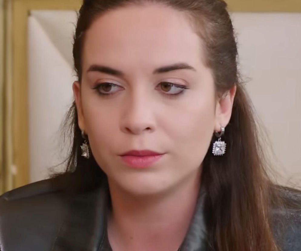 Aktorka Talya Çelebi, grająca Hançer w serialu Panna młoda, spogląda w bok z poważną miną. Ma brązowe włosy upięte w koński ogon i kolczyki z kryształkami. Postać Hançer jest kluczowa dla fabuły, o której więcej przeczytasz na Super Seriale.