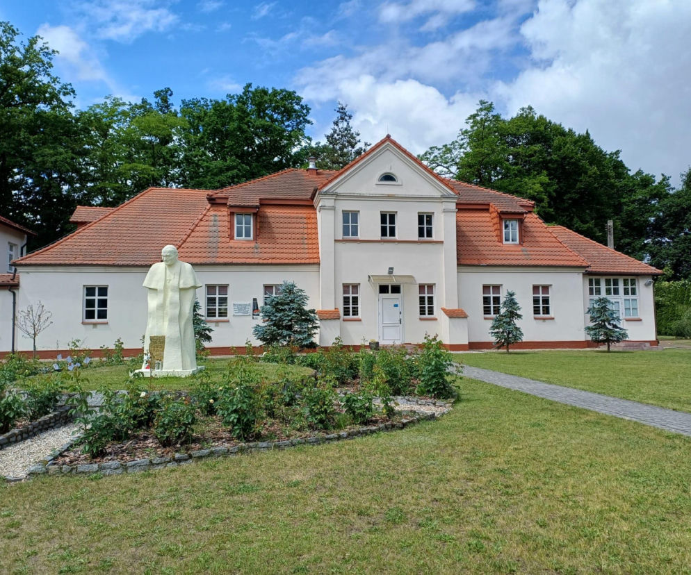 Budynek szkoły w gminie Kraszewice z pomnikiem Jana Pawła II. O projekcie z funduszy UE dowiesz się z Eska Ostrzeszów.