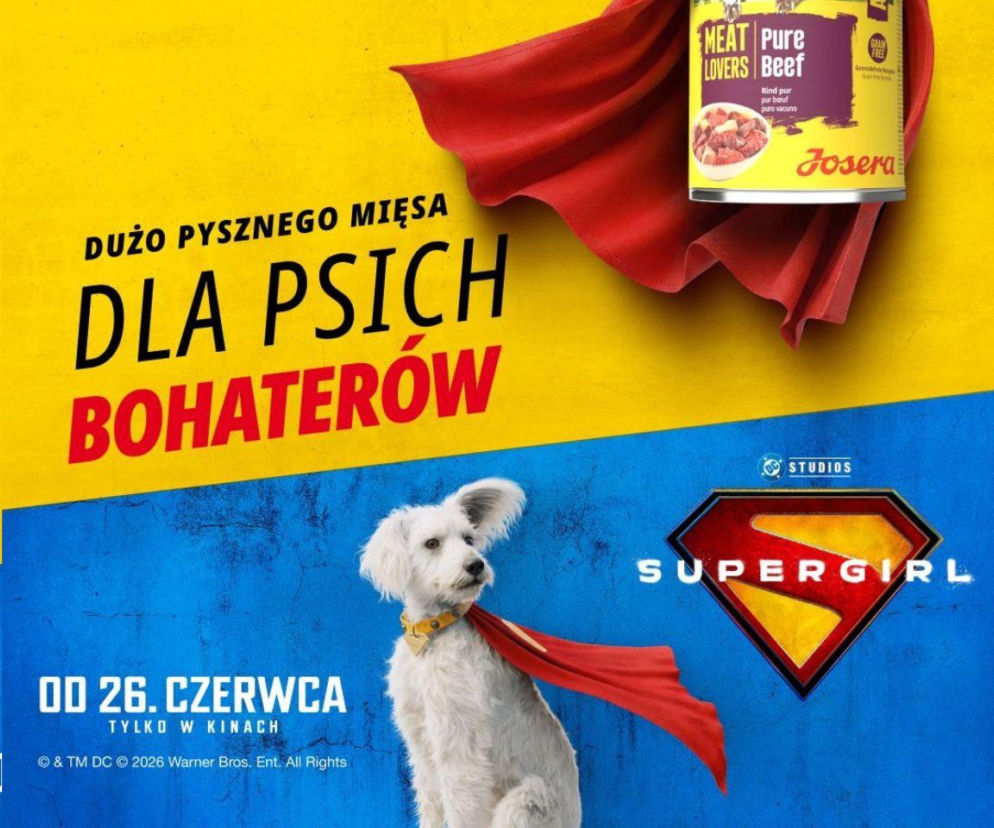 Biały pies w czerwonej pelerynie, wyglądający jak superbohater, stoi obok puszki karmy Josera Meat Pure Lovers Beef, promując kampanię Josera Supergirl. Na żółto-niebieskim tle widnieje hasło Dużo pysznego mięsa dla psich bohaterów oraz informacja o premierze filmu 26 czerwca, o której możesz przeczytać na naszym portalu.