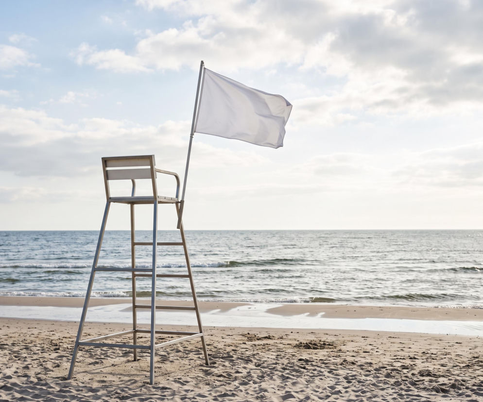 Biała flaga powiewająca przy wieży ratowniczej na pustej plaży w Niechorzu. O warunkach kąpieli przeczytasz na SE Szczecin.