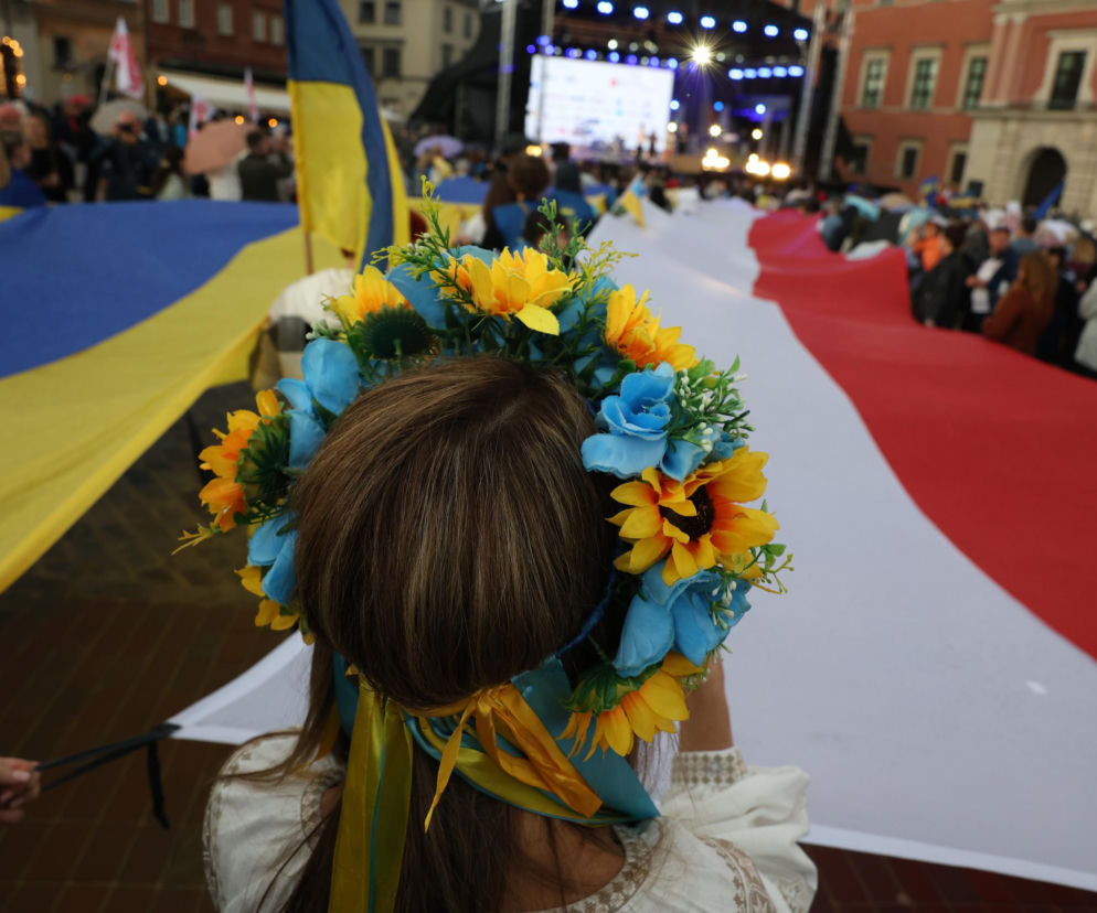 Dziewczynka w wianku patrzy na flagi Polski i Ukrainy. O obchodach na Placu Zamkowym przeczytasz w Eska Warszawa.