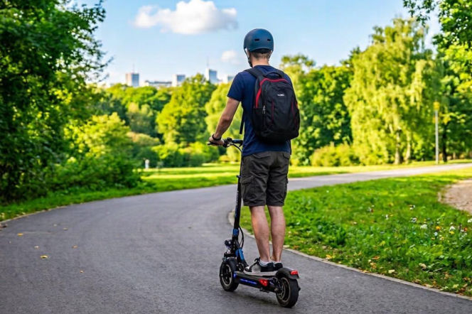 Mężczyzna w kasku jadący hulajnogą elektryczną przez park. O zasadach bezpieczeństwa przeczytasz na Eska Nowy-Sącz.
