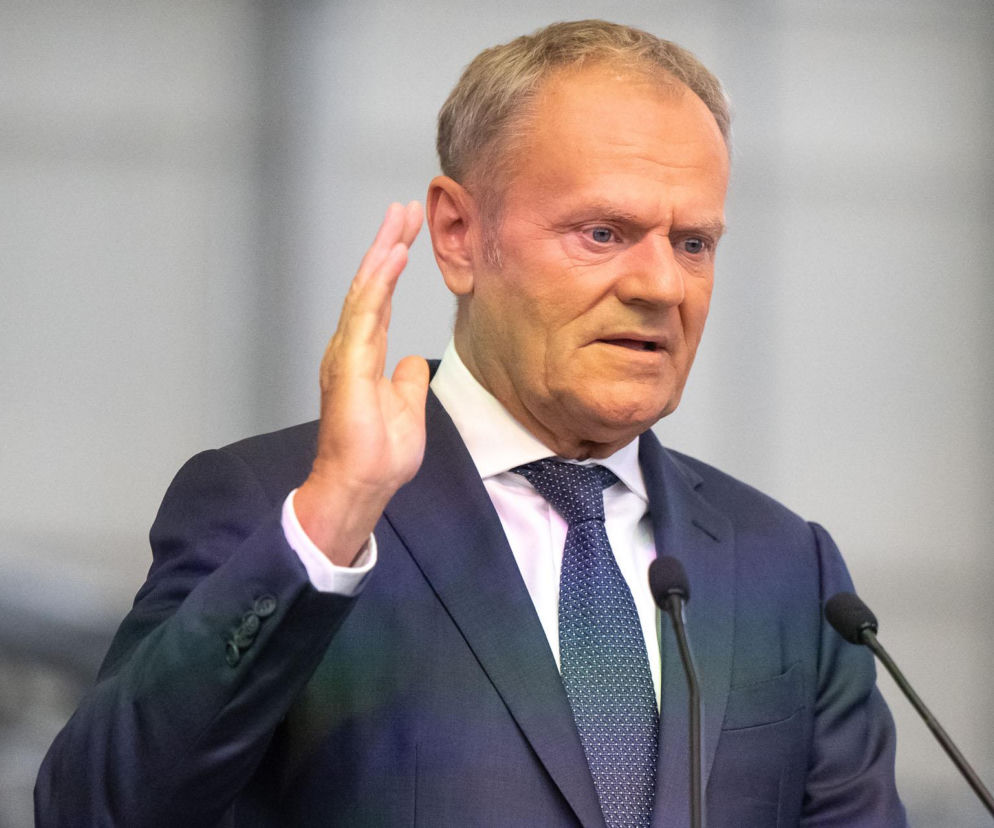 Premier Donald Tusk przemawia przy mikrofonach, podnosząc prawą rękę. O programie CPN przeczytasz na SE Superbiz.