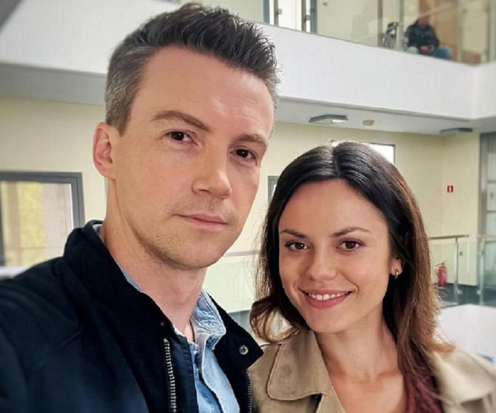 Aktor Krzysztof Kwiatkowski, grający Jakuba Karskiego w M jak miłość, pozuje do zdjęcia z uśmiechniętą Kingą Głuc, aktorką znaną z serialu Hotel 52. Para robi selfie w jasnym wnętrzu, być może na planie, co potwierdza ich obecność w świecie Super Seriale.