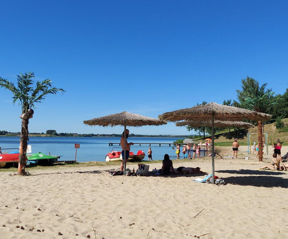 Piaszczysta plaża nad zalewem pod Zamościem ze słomianymi parasolami i rowerami wodnymi. Więcej na SE Lublin.