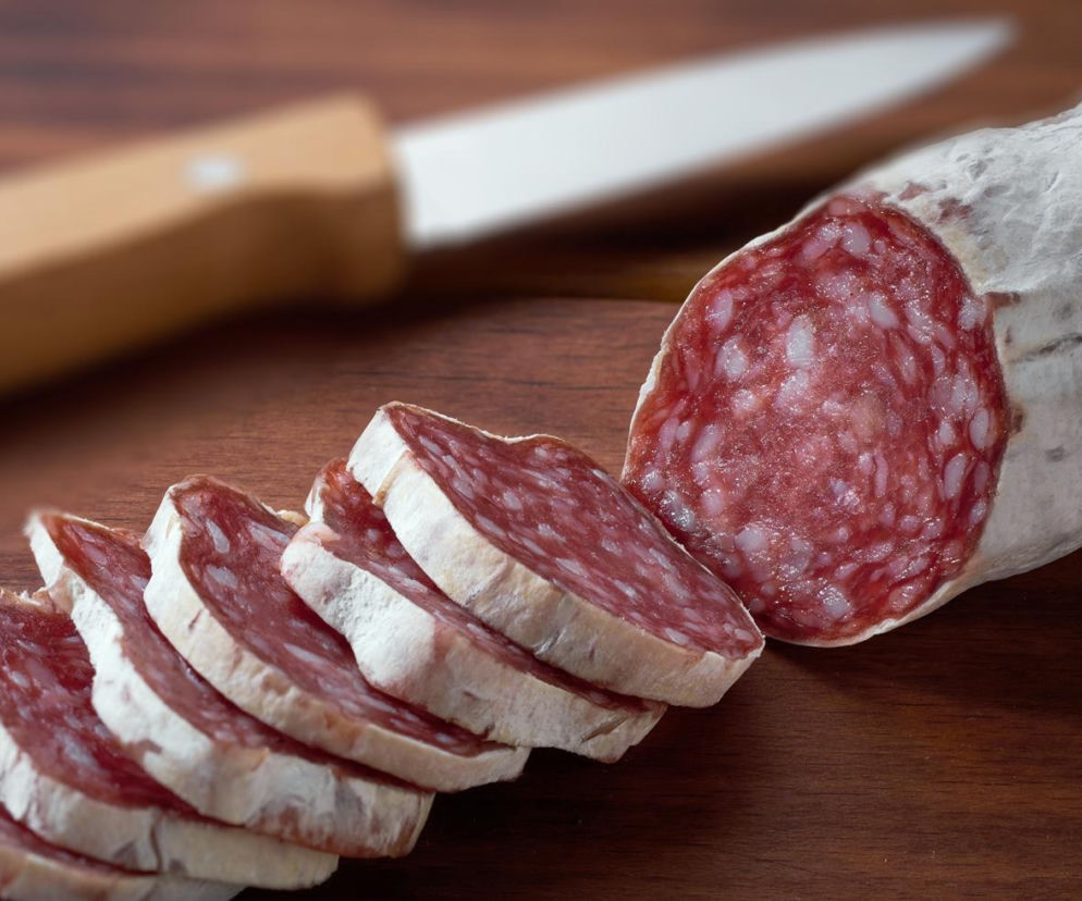 Pokrojone w plastry salami na drewnianej desce. O wycofaniu skażonych partii wędlin przez GIS przeczytasz na Eska.