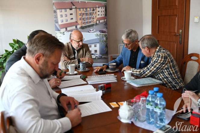 Mężczyźni przy stole podczas podpisywania umowy. W tle projekt bloku. O nowej inwestycji w Sławie czytaj w Eska Leszno.