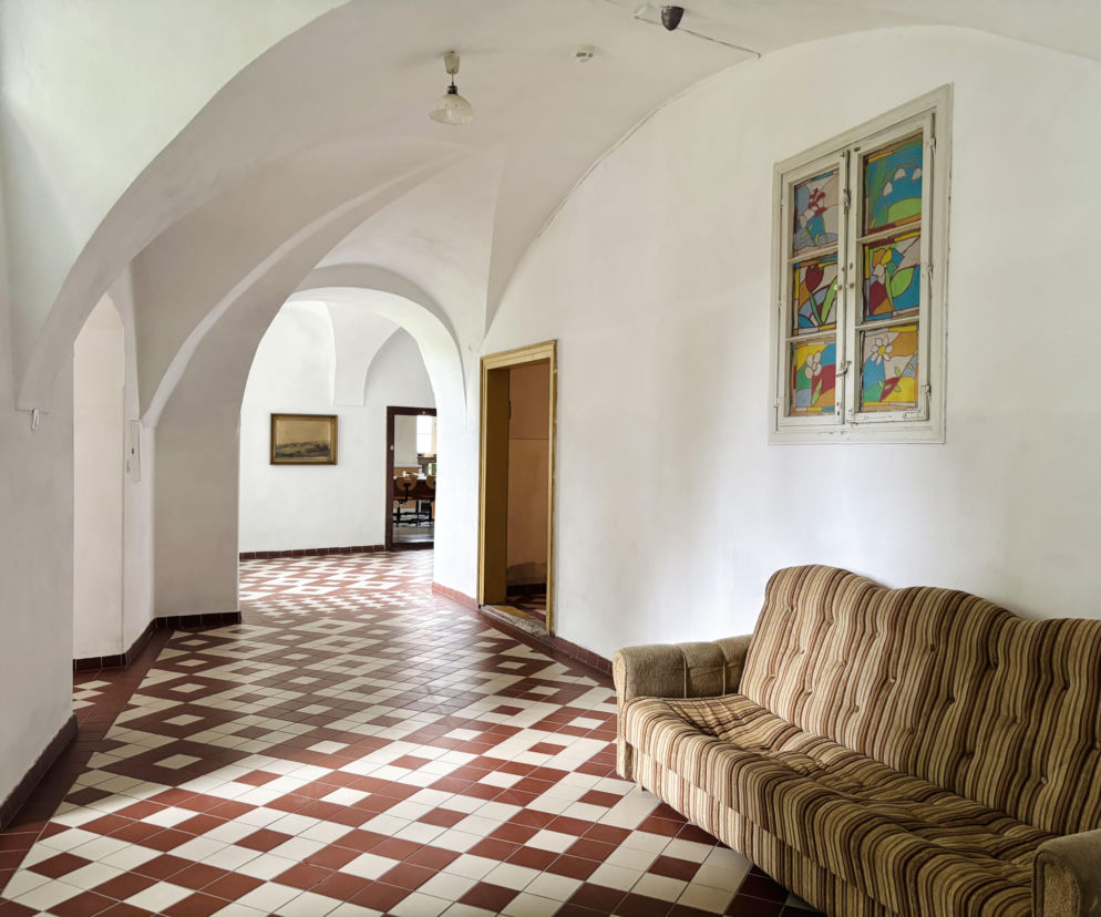 Biały korytarz klasztoru ze sklepieniami, sofą i witrażem. O rewitalizacji w Lubomierzu przeczytasz na Architektura.