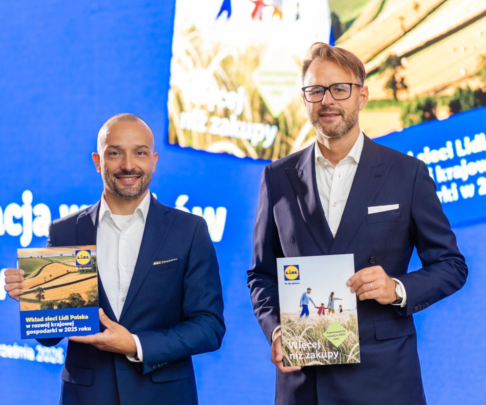 Dwaj uśmiechnięci mężczyźni w garniturach trzymają raporty Lidl Polska. O wpływie sieci na PKB czytaj na SE Superbiz.