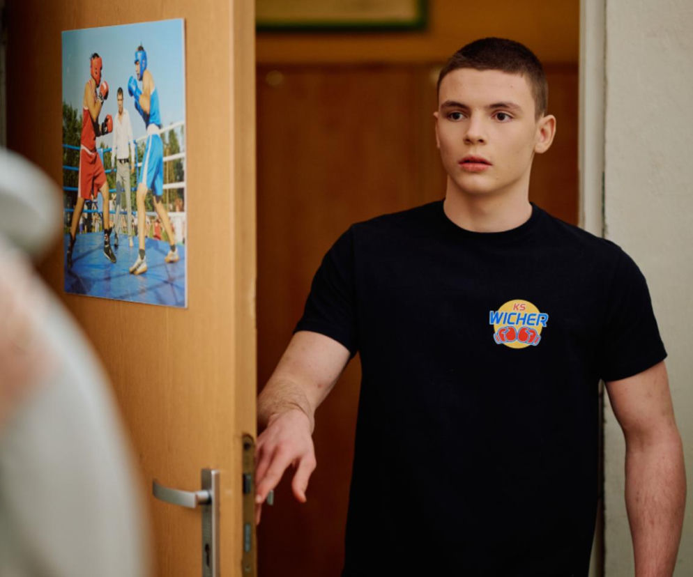 Zaskoczony Junior z serialu Na Wspólnej stoi w drzwiach pokoju. O buncie bohatera przeczytasz na SE Superseriale.