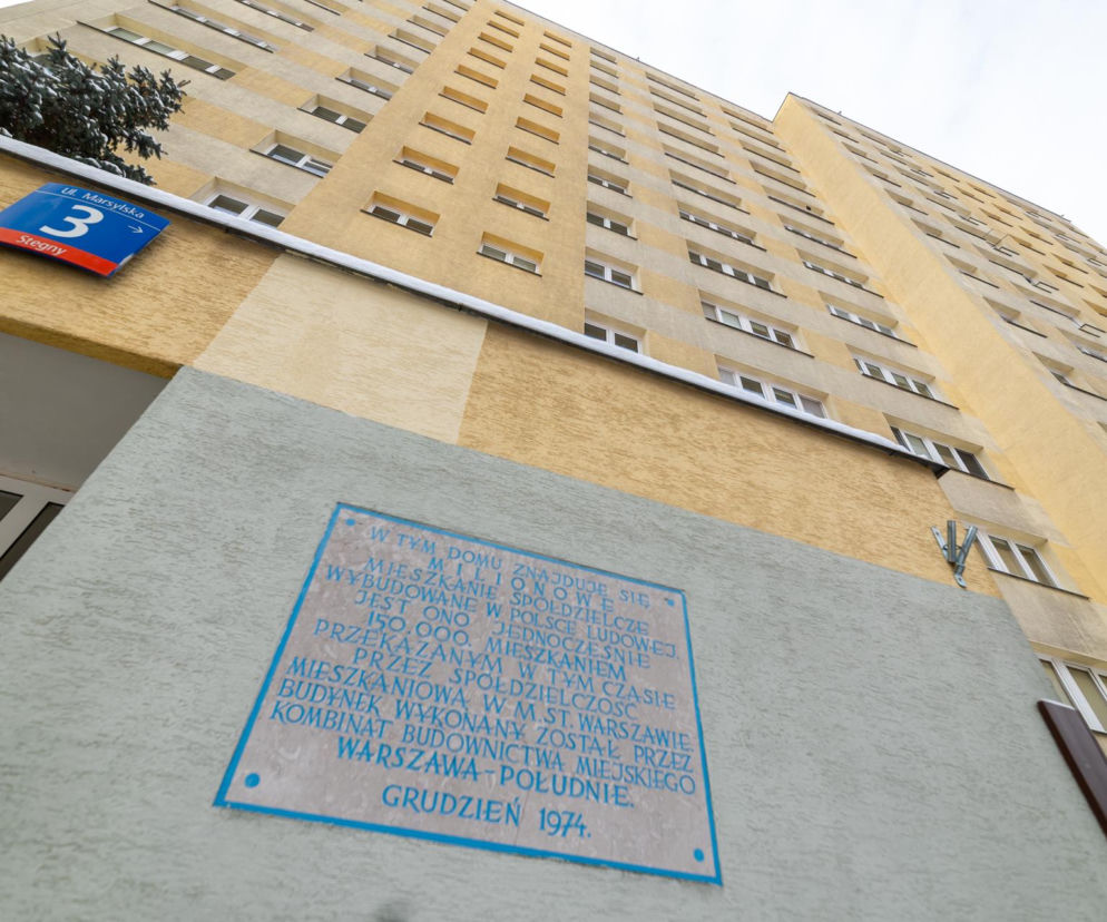 Wysoki blok z wielkiej płyty na warszawskim osiedlu Stegny, przy ulicy Marsylskiej 3. Na budynku tablica upamiętniająca milionowe mieszkanie spółdzielcze w PRL. Obok wejścia do klatki śnieg na zielonych iglakach i numer adresu. Więcej o architekturze minionych lat na Architektura Murator Plus.