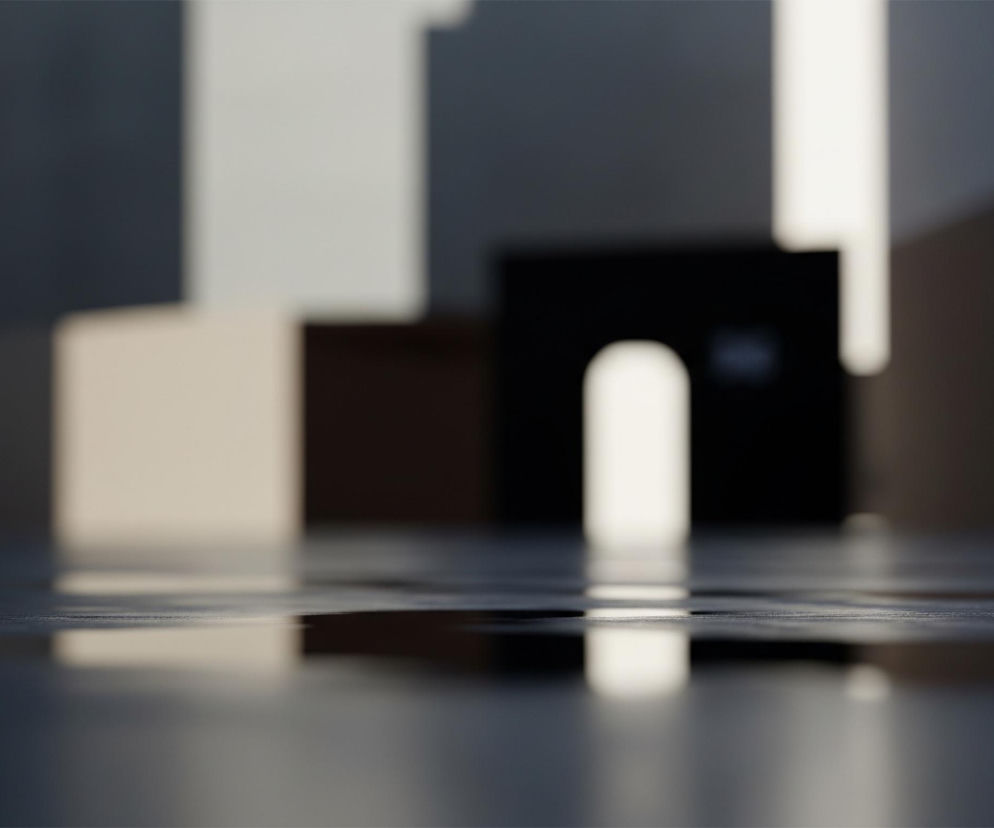 Ujęcia ukazuje rozmyte, abstrakcyjne tło z wyraźnym odbiciem w błyszczącej, ciemnej powierzchni na pierwszym planie. Na tle dominują kształty przypominające bloki i prostopadłościany, głównie w odcieniach szarości, czerni i beżu, z jasnymi smugami światła tworzącymi pionowe i poziome paski. Centralnie, w tle, widoczny jest czarny sześcian z wyraźnym, jasnym łukowatym otworem, stanowiącym punkt ogniskowy rozmytego światła. Całość jest skąpana w kontrastowym oświetleniu, które tworzy głębokie cienie i jasne plamy.