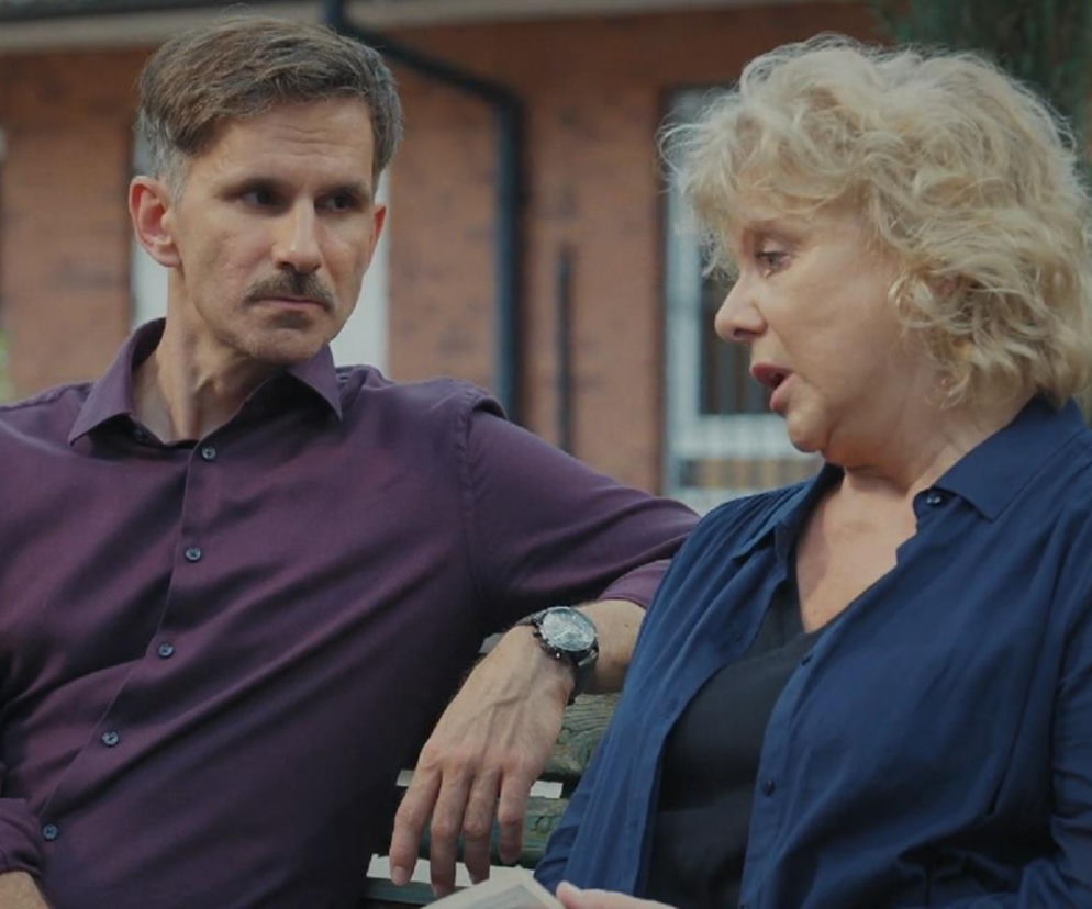 Aktor Marcin Bosak jako Kamil w fioletowej koszuli i Dorota Kamińska jako Anna Lerman w granatowej koszuli, siedzący na ławce. Kamil uważnie słucha Anny, która z przejęciem opowiada o swoim problemie z uzależnieniem. Więcej o ich losach na stronie Super Seriale.