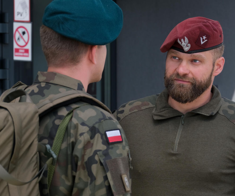 Tomasz Rożniatowski, weteran z Afganistanu, znany z M jak miłość, w stroju wojskowym z bordowym beretem, rozmawiający z innym żołnierzem odwróconym plecami. Fotografia ukazująca prawdziwe przeżycia wojskowe, o których można przeczytać na Super Seriale.