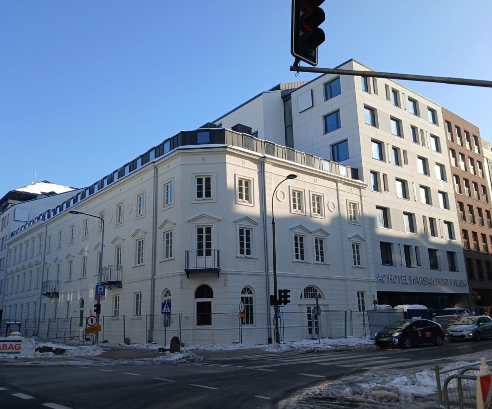 Odrestaurowana kamienica Karola Mintera na rogu ulic Sierakowskiego i Okrzei w Warszawie, stanowiąca część powstającego hotelu AC Hotel Warsaw Port Praski. Biała, odnowiona elewacja zabytku z widocznymi oknami i balkonem, obok nowoczesna zabudowa, uzupełniająca kompleks. Więcej o architekturze na portalu Architektura Murator Plus.