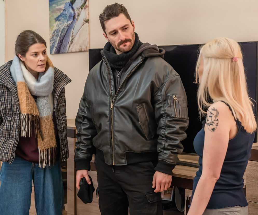 Aktorki i aktor, prawdopodobnie z serialu Sprawiedliwi. Trójmiasto, prowadzą intensywną rozmowę, stojąc w jasnym pomieszczeniu. Kobieta po lewej w kurtce i szalu, mężczyzna w czarnej kurtce, a blondynka tyłem z tatuażem na ramieniu. O tej scenie i innych odcinkach przeczytasz na Super Seriale.