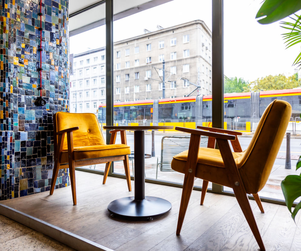 Dwa żółte fotele i stolik w kawiarni obok mozaikowego filara. O zabytkowym wnętrzu na Mokotowie przeczytasz na Architektura.