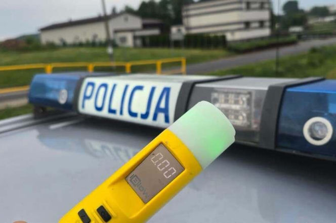 Żółty alkomat na tle dachu radiowozu z napisem Policja. O pijanym policjancie z Zawiercia przeczytasz na SE.