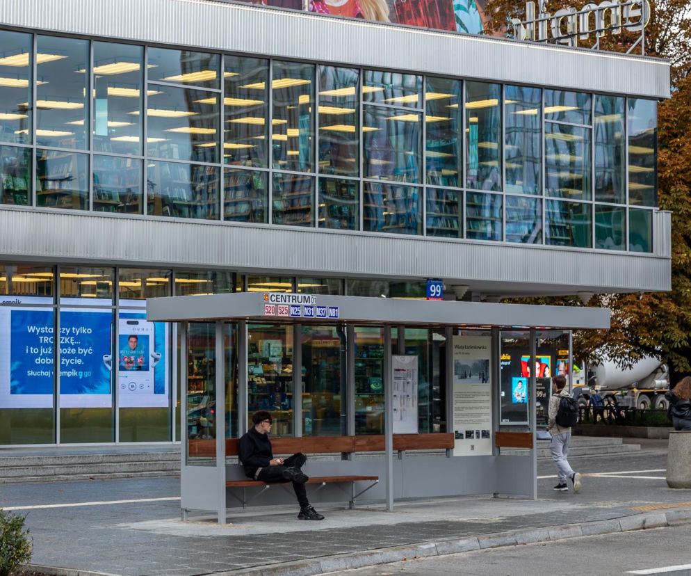 Odrestaurowana szara wiata przystankowa typu Ełka przed przeszklonym budynkiem Empiku. O designie PRL przeczytasz w Architektura.