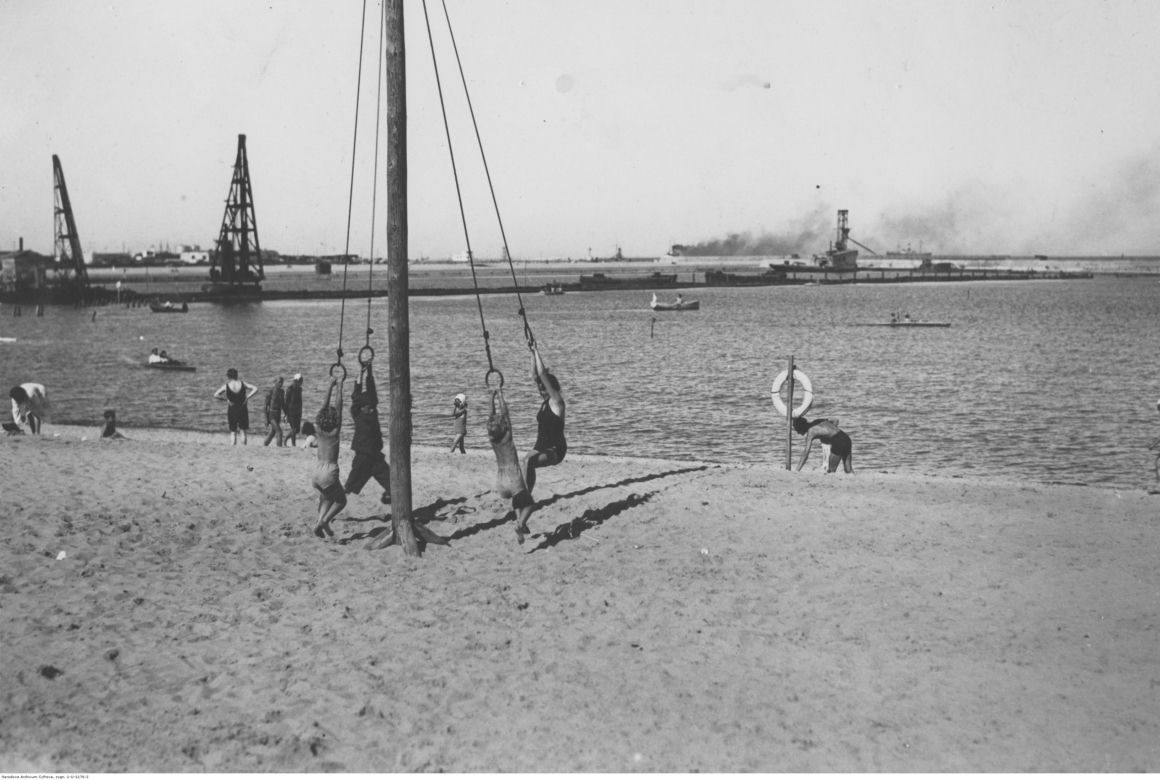 Dzieci na huśtawce na plaży nad morzem Bałtyckim. W tle fragment portu. Miejsce zrobienia zdjęcia Gdynia w okresie 1923-1939