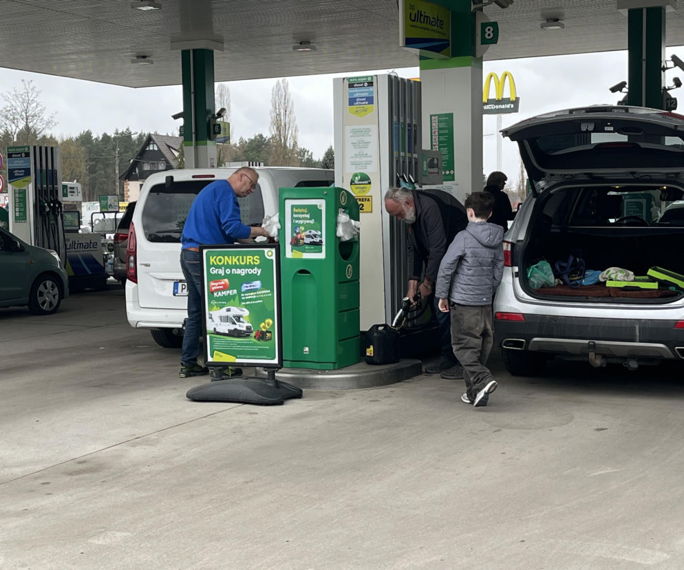 Mężczyźni tankujący paliwo na stacji benzynowej BP, w tle szyld McDonald's, co odzwierciedla codzienne życie konsumentów i kwestie oszczędności po obniżeniu cen. Więcej o wpływie polityki rządu Donalda Tuska na portfele Polaków i ceny paliw przeczytasz na portalu Super Biznes.