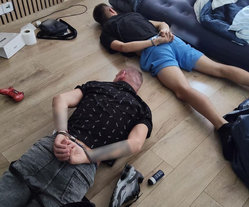 Dwóch mężczyzn w kajdankach leżących na drewnianej podłodze, zatrzymanych przez policję w Bydgoszczy w związku z likwidacją magazynu narkotyków. O sprawie przeczytasz więcej na naszym portalu.