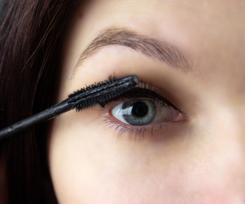 Zbliżenie na oko kobiety, która nakłada czarny tusz do rzęs, podkreślając ich długość i objętość. Zdjęcie ilustruje znaczenie prawidłowego używania kosmetyków do makijażu oczu oraz przestrzegania terminu ważności, o czym przeczytasz więcej na Poradnik Zdrowie.
