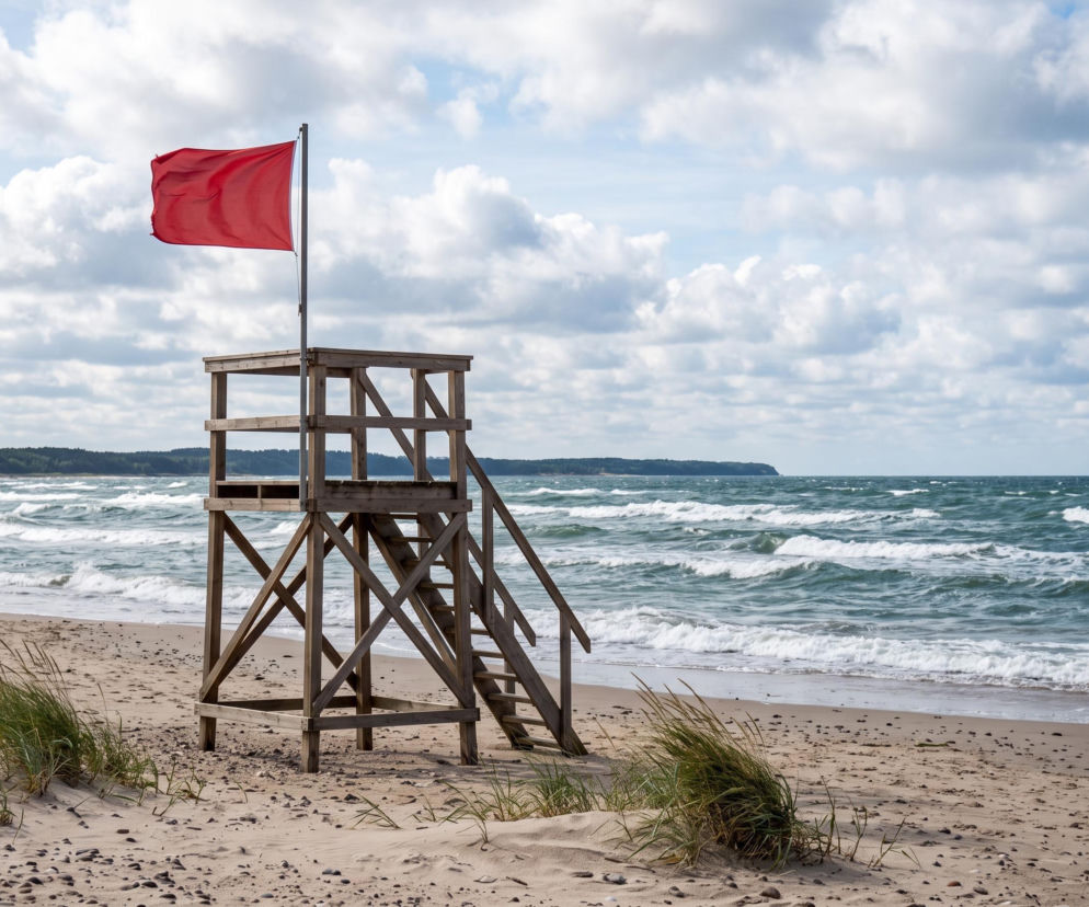 Drewniana wieża ratownicza na plaży z powiewającą czerwoną flagą. O bezpieczeństwie w Sarbinowie przeczytasz na SE Szczecin.