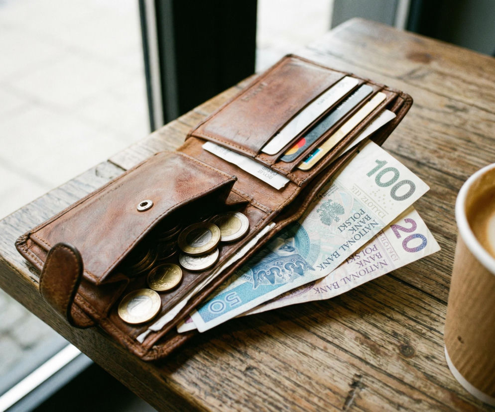 Otwarty portfel z polskimi banknotami i monetami na drewnianym stole. O nastrojach konsumentów przeczytasz w Eskalo.