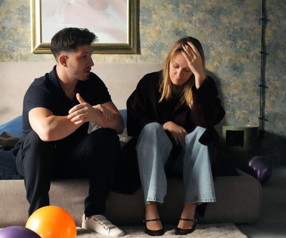 Justin (Jasper Sołtysiewicz) i Ola (Michalina Robakiewicz) w scenie z serialu Barwy szczęścia. Justin siedzi na łóżku, rozmawiając z siedzącą obok Olą, która opiera głowę na ręce, sprawiając wrażenie zmartwionej. W tle obraz na ścianie i bukiet tulipanów. Więcej o ich losach na Super Seriale.