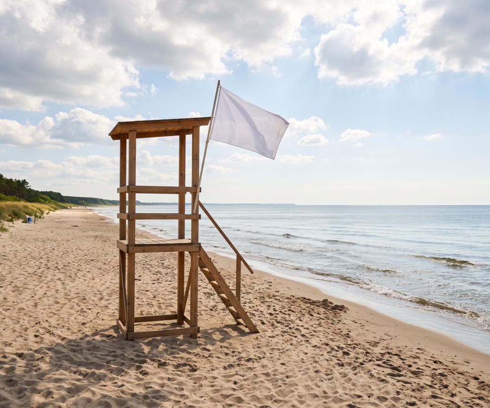Drewniana wieża ratownicza z białą flagą na pustej plaży w Niechorzu. O bezpieczeństwie nad wodą czytaj w SE Szczecin.