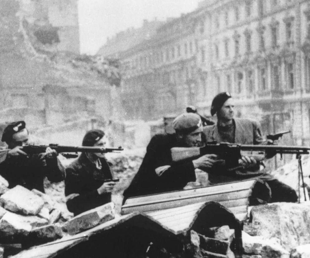Czterej uzbrojeni powstańcy warszawscy na barykadzie wśród ruin. O walkach na Starówce przeczytasz w serwisie Eska.