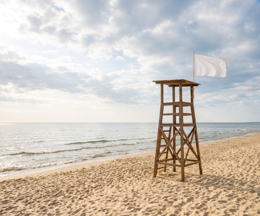 Drewniana wieża ratownika z białą flagą na pustej plaży. O bezpiecznej kąpieli w Międzyzdrojach przeczytasz na SE Szczecin.
