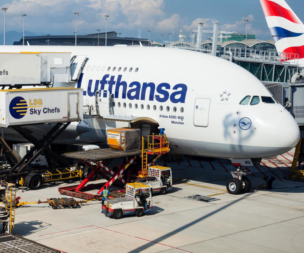 Samolot Lufthansa A380-800 na płycie lotniska podczas załadunku bagaży i cateringu. Maszyna szykuje się do rejsu, a ten artykuł na Super Biznes informuje o zmianach w zasadach dotyczących bagażu podręcznego u niemieckiego przewoźnika.