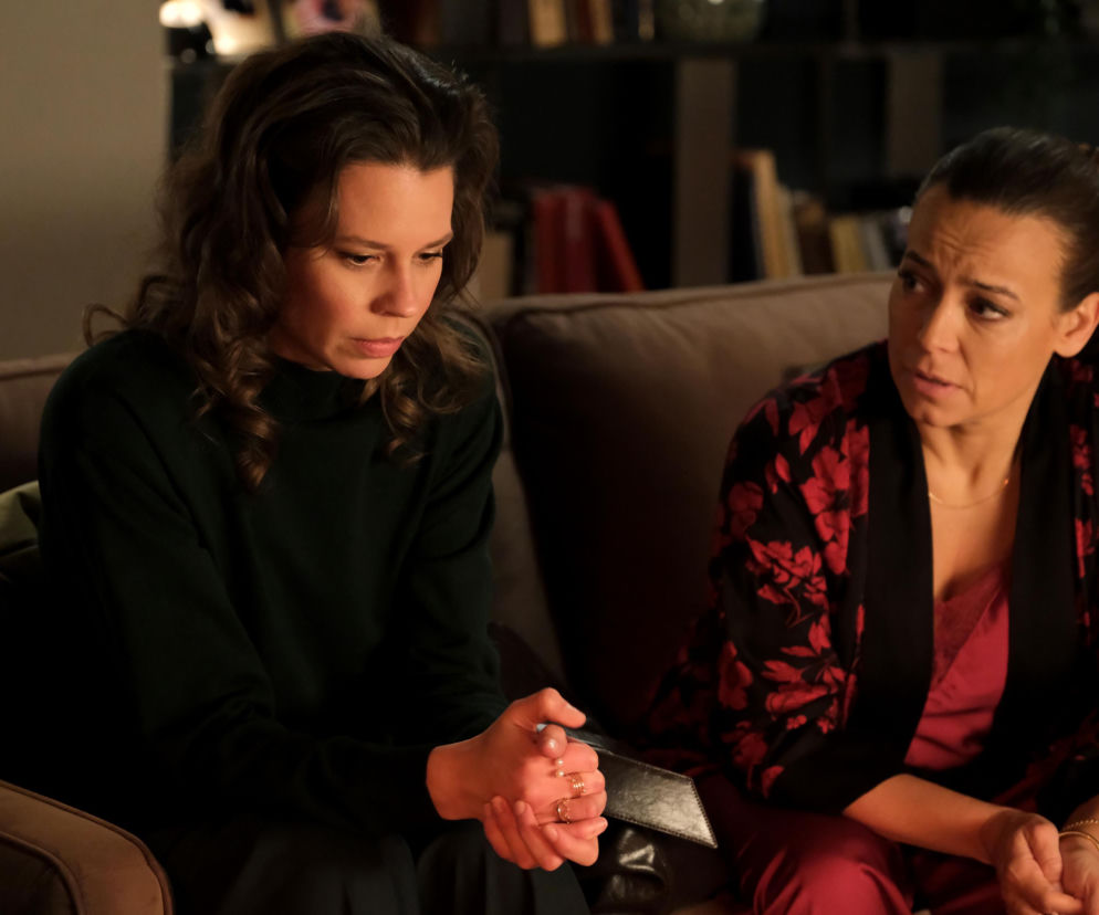 Paulina Lipska (Maria Wieczorek) z zamyśloną miną, siedząca na kanapie obok Magdy Budzyńskiej (Anna Mucha), która spogląda na nią z zatroskaniem. Scena przedstawia emocje związane z powrotem Pauliny w 1933 odcinku „M jak miłość”, o czym więcej przeczytasz na Super Seriale.