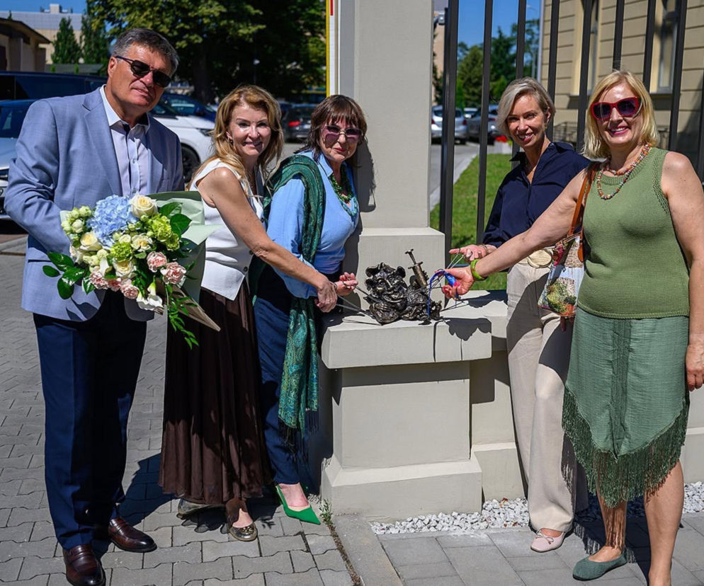 Uroczyste odsłonięcie figurki maszkarona Szpitalnika w Tarnowie, z udziałem pięciu osób: mężczyzny w jasnym garniturze z bukietem kwiatów oraz czterech uśmiechniętych kobiet, w tym Małgorzaty Mękal i autorki projektu Ewy Fleszar, które symbolicznie odsłaniają nową rzeźbę. O tym wydarzeniu przeczytasz więcej na naszym portalu.