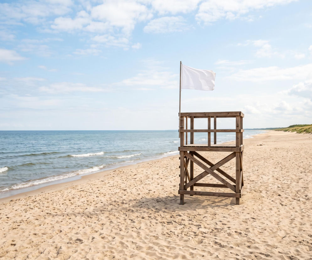 Drewniana wieża ratownicza z białą flagą na pustej plaży w Grzybowie. O bezpieczeństwie nad wodą czytaj w SE Szczecin.