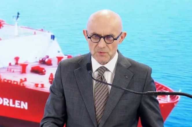 Prezes Orlenu Ireneusz Fąfara w okularach, ubrany w garnitur i krawat, przemawia do mikrofonu na tle statku z logo Orlen. Mówi o stabilności cen gazu w Polsce, co jest istotną informacją do przeczytania na portalu Super Biznes.