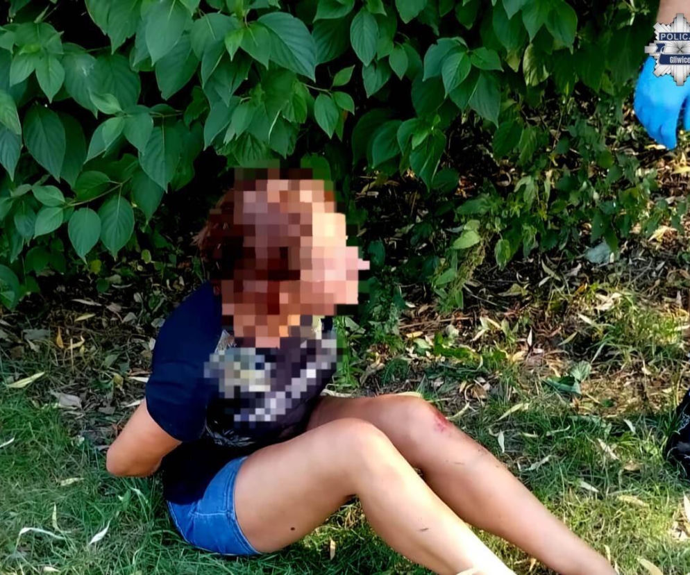 Kobieta z zakrytą twarzą siedzi na trawie obok policjanta. O pijanej kierującej z Gliwic przeczytasz na SE.