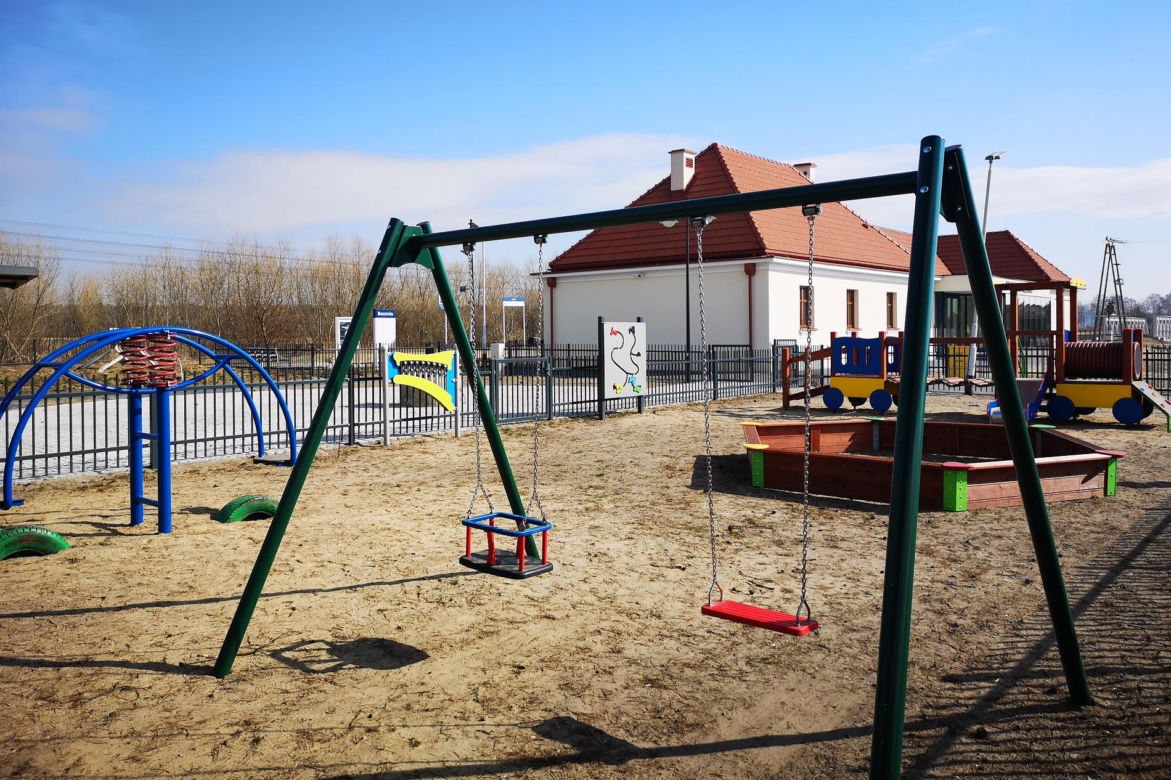Nowy plac zabaw z odnowionym budynkiem stacji w tle