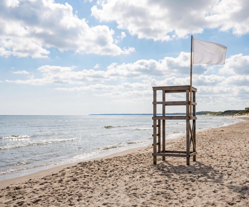 Drewniana wieża ratownika z białą flagą na plaży w Łazach nad Bałtykiem. O warunkach kąpieli przeczytasz na SE Szczecin.