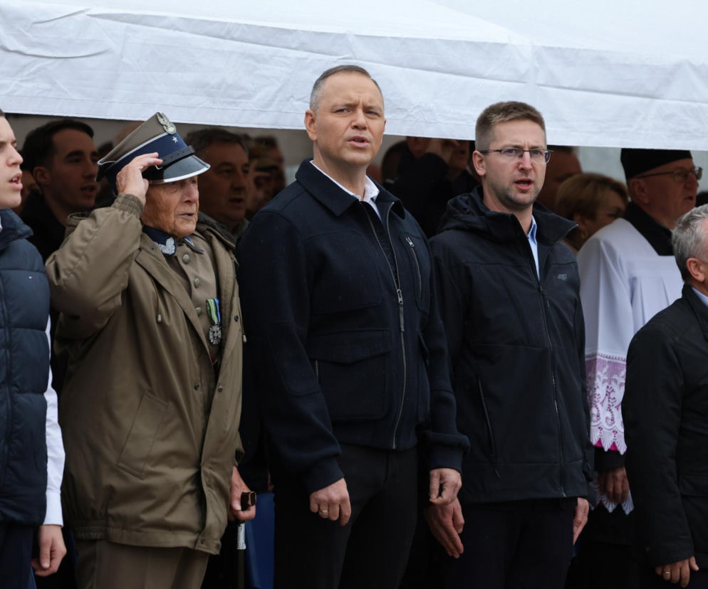 Karol Nawrocki stoi pod białym namiotem obok salutującego żołnierza. O debacie o broni przeczytasz na SE Polityka.