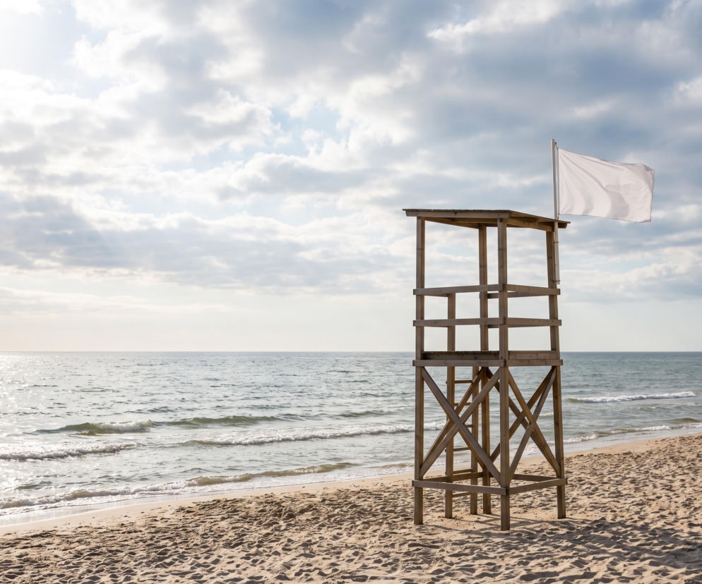 Drewniana wieża ratownicza z białą flagą na plaży w Mielnie. O warunkach nad morzem przeczytasz na SE Szczecin.