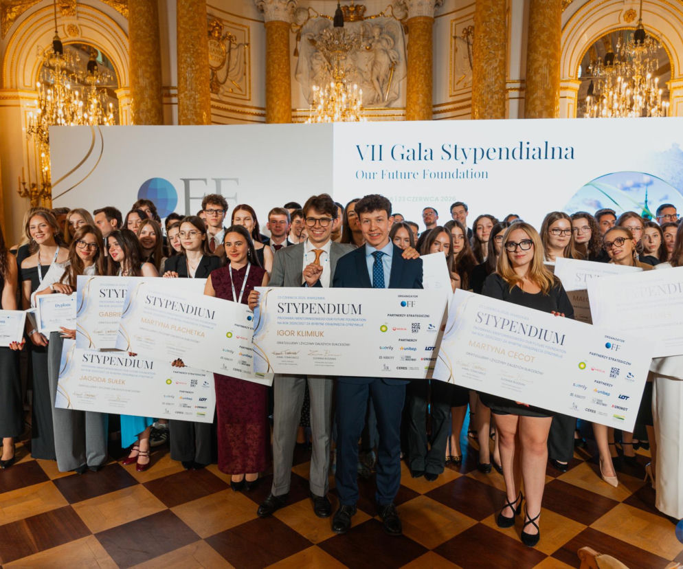 Grupa młodych, uśmiechniętych laureatów, ubranych w eleganckie stroje, trzymających duże dyplomy stypendialne, pozuje na tle eleganckiej, jasno oświetlonej sali z kryształowymi żyrandolami i logiem VII Gala Stypendialna Our Future Foundation. Na portalu Poradnik Zdrowie można znaleźć więcej informacji o młodych talentach.