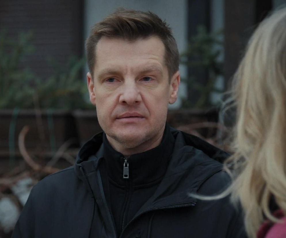 Paweł Zduński (Rafał Mroczek) w czarnej kurtce z kapturem, z zamyśloną twarzą, rozmawia z niewidoczną od przodu blondwłosą kobietą (Judyta Kosowska, Paulina Chruściel) na zewnątrz. To kadr z serialu M jak miłość, o którym więcej przeczytasz na portalu Super Seriale.