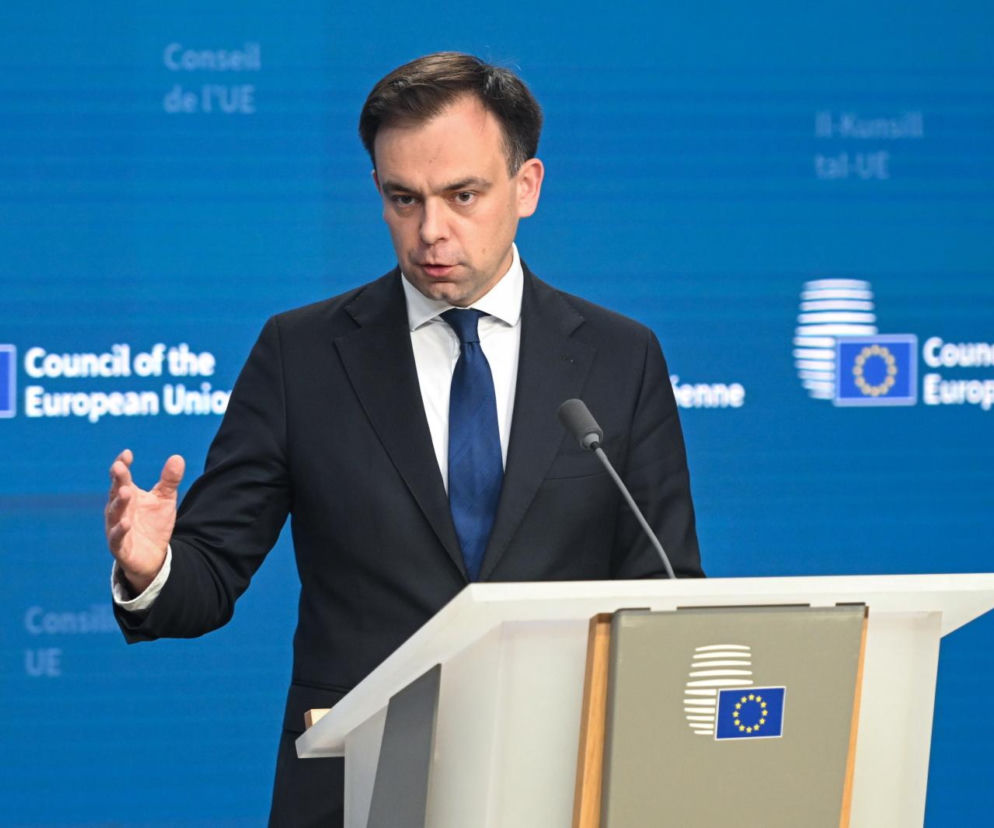 Minister finansów Andrzej Domański przemawia przy pulpicie na tle logo Rady UE. O danych GUS pisze SE Superbiz.