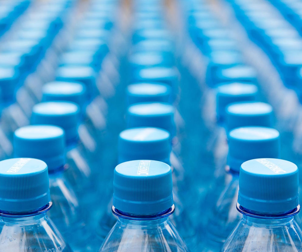 Rzędy plastikowych butelek z błękitnymi zakrętkami. O kontrowersjach wokół systemu kaucyjnego przeczytasz na Eska.